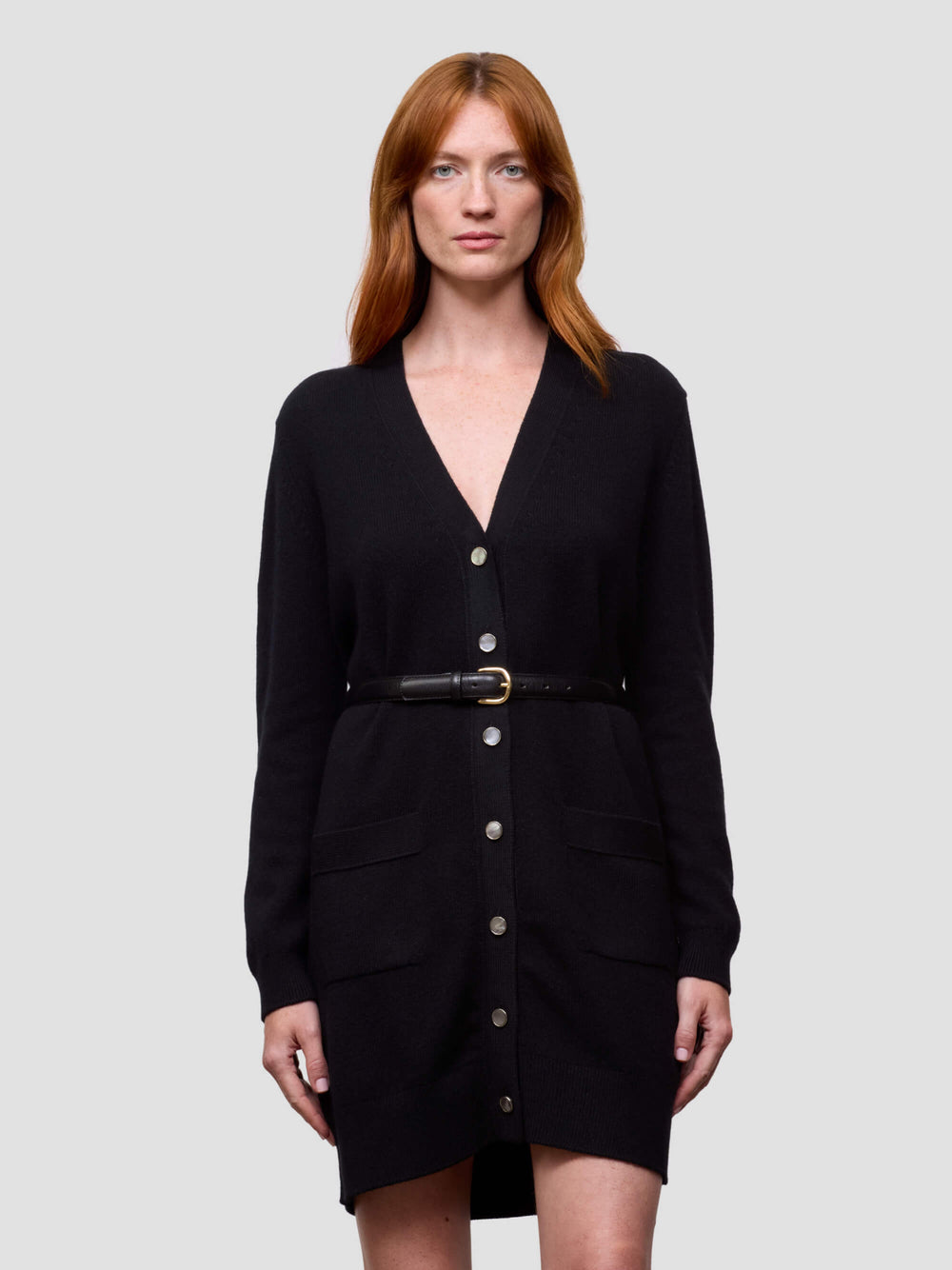 Woman wearing a black cashmere cardigan dress with a belt on a light gray background