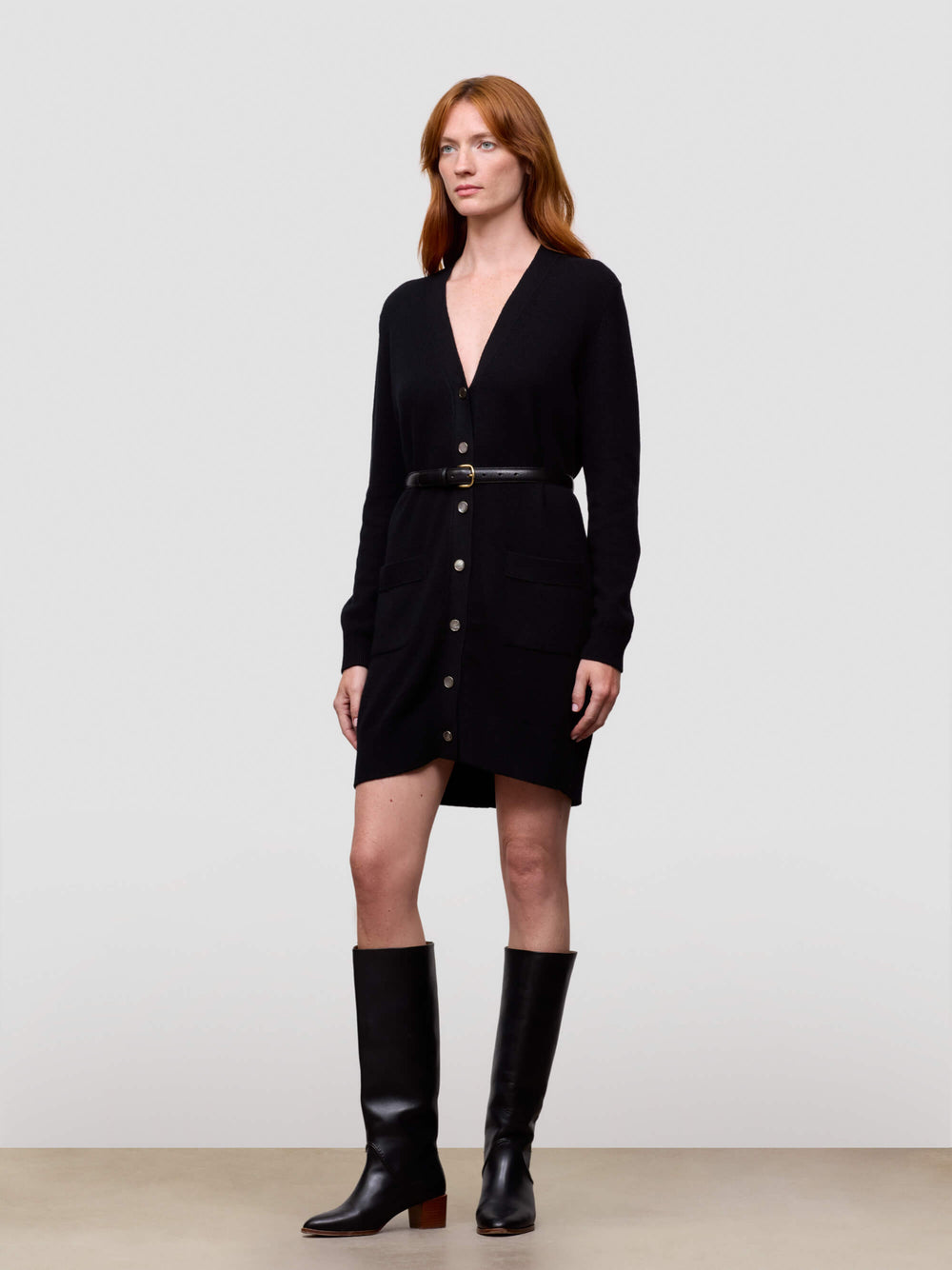 Woman wearing a long black cashmere cardigan with buttons and black knee-high boots on a white background