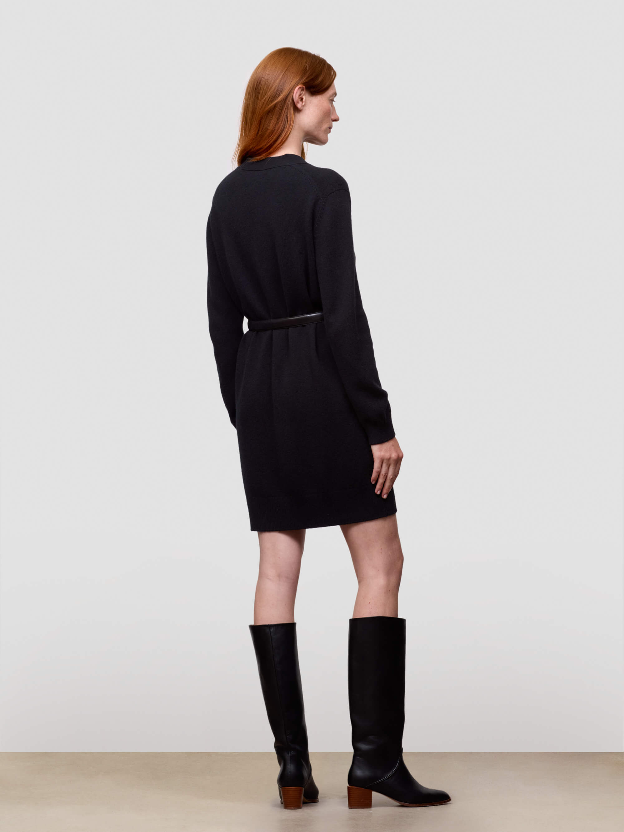 Woman wearing a long black cashmere cardigan and black knee-high boots on a white background
