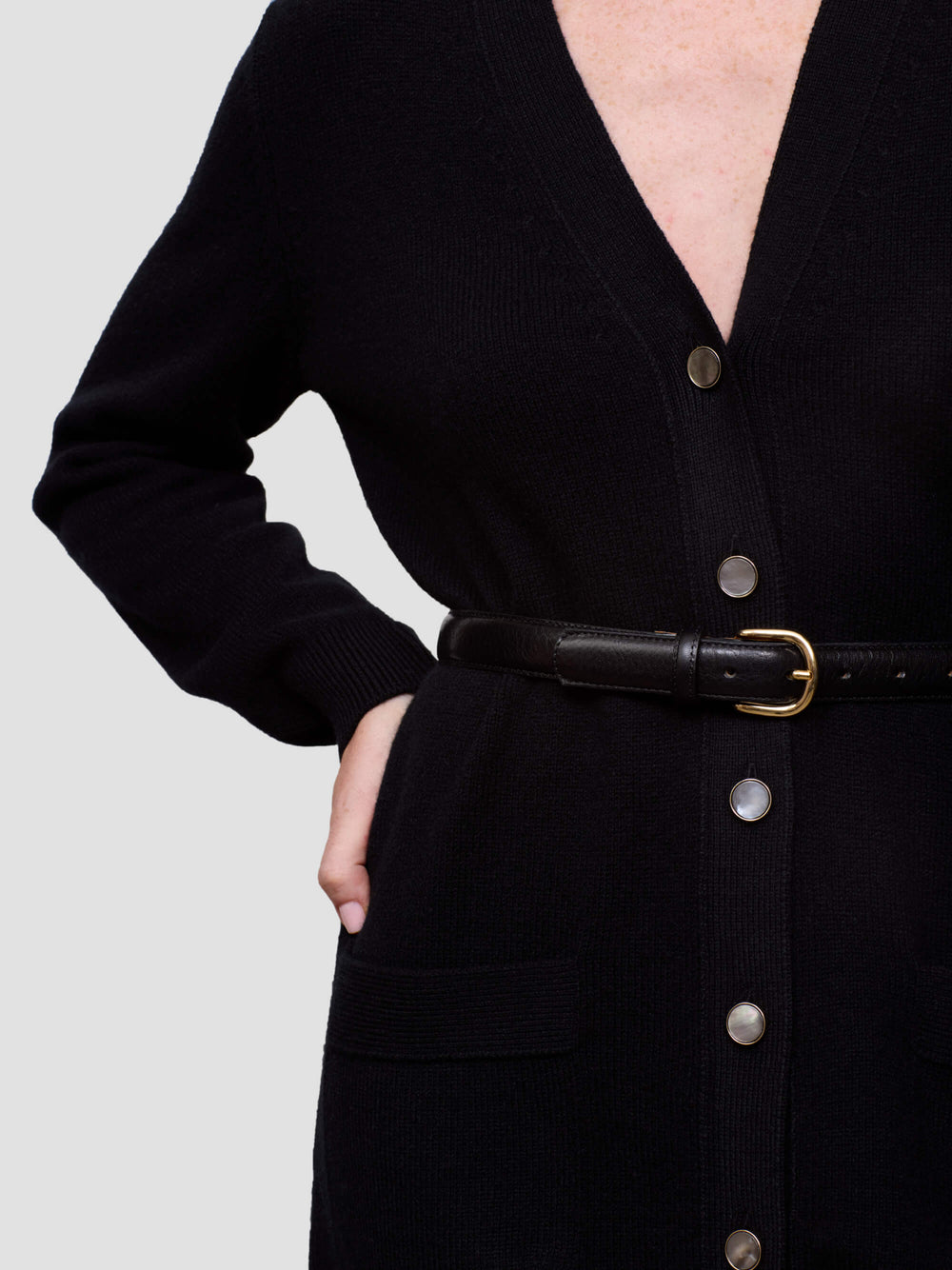 Black button-up cashmere dress with a belt on a plain background