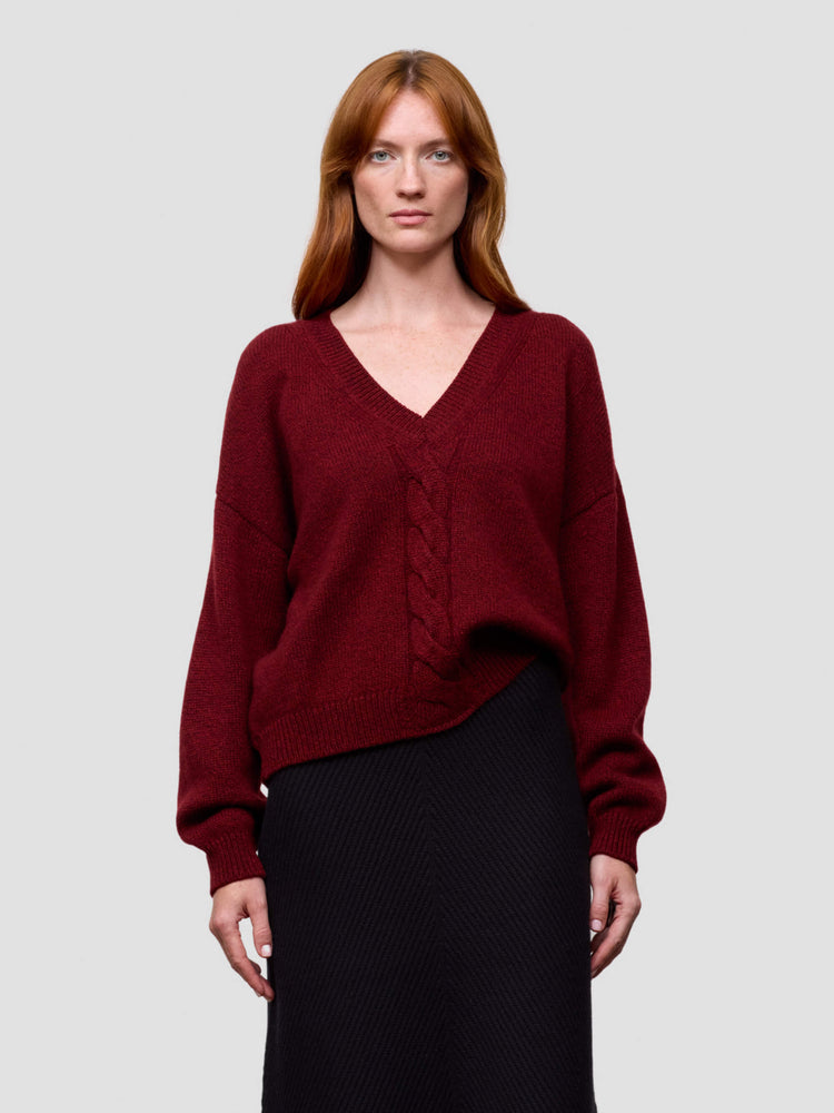 woman wearing a red chunky v-neck cashmere sweater and black cashmere skirt on a grey background