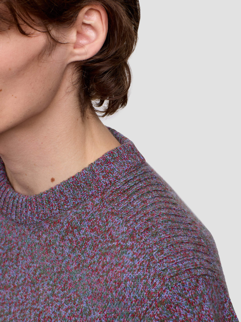 Man wearing a patterned purple cashmere sweater and black pants on a plain background