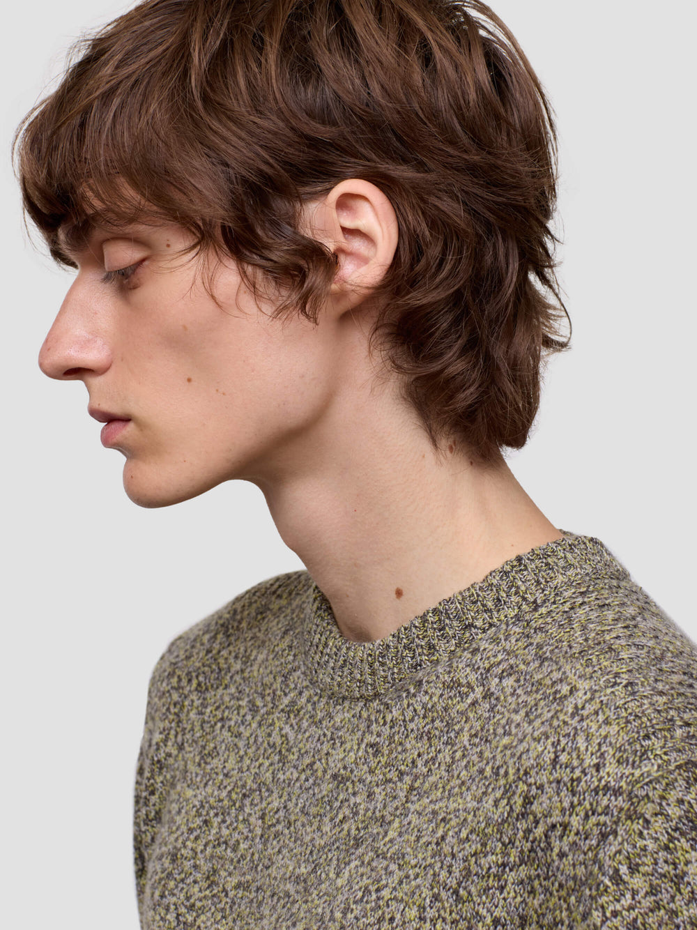 close up of man wearing a patterned green cashmere sweater and dark pants on a plain background