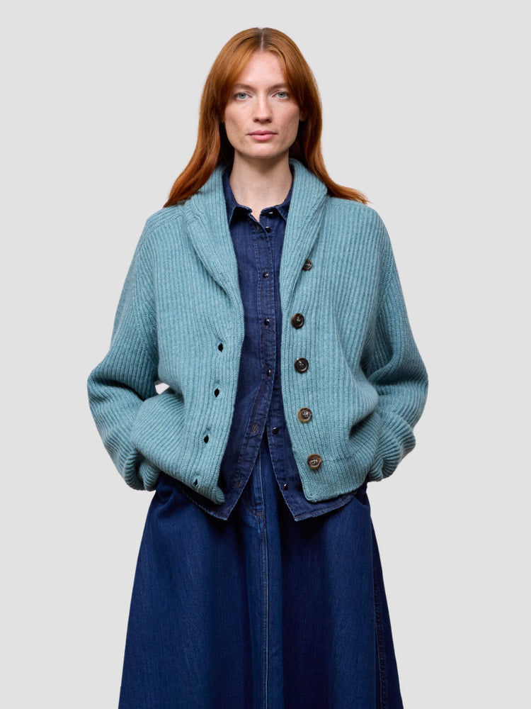 Woman wearing a teal knitted cashmere cardigan over a blue dress on a light gray background