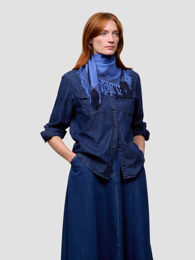 Woman wearing a blue denim outfit with a matching blue cashmere scarf scarf on a light gray background