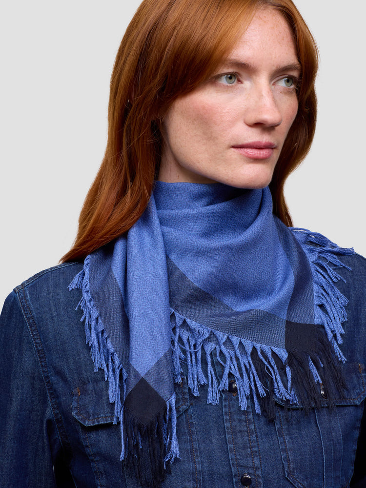 Woman wearing a blue cashmere scarf with fringe details on a plain background