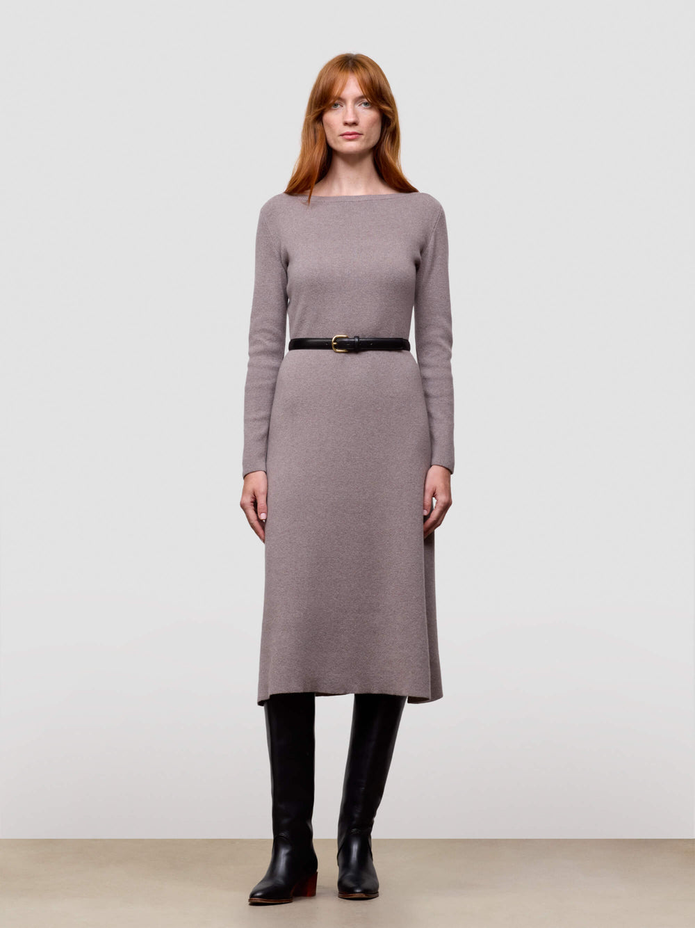 Woman wearing a grey long-sleeve cashmere dress with a belt against a plain background
