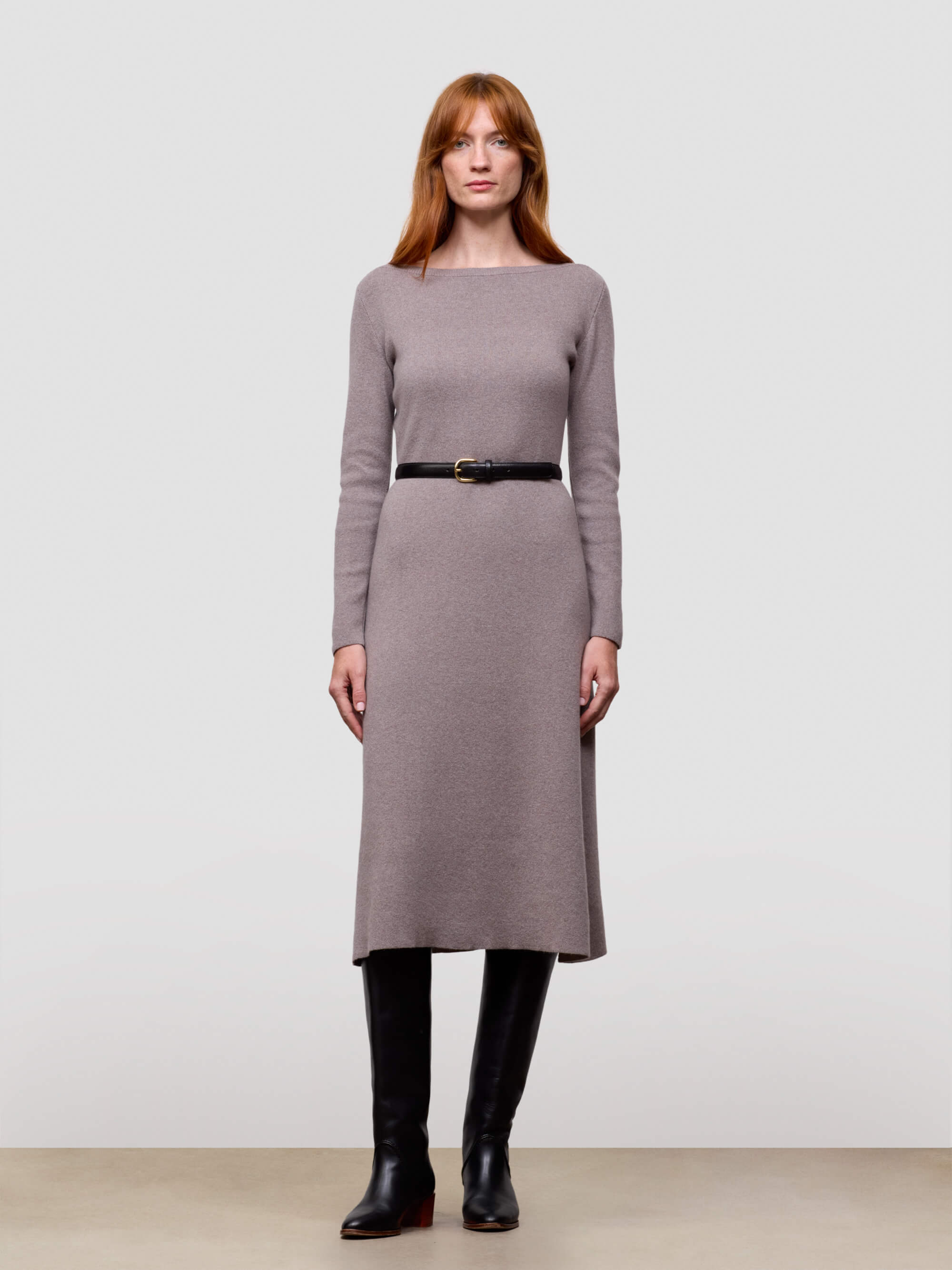 Woman wearing a grey long-sleeve cashmere dress with a belt against a plain background
