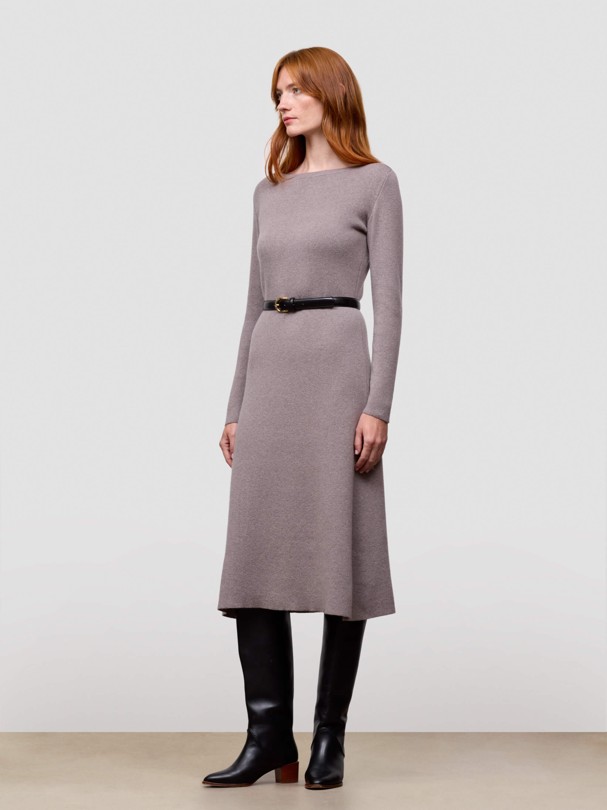 Woman wearing a grey long-sleeve cashmere dress with a belt against a plain background