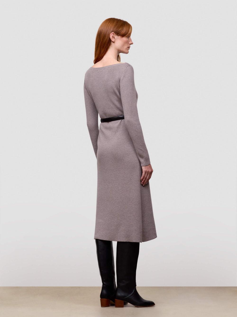 Woman wearing a grey long-sleeve cashmere dress with a belt against a plain background