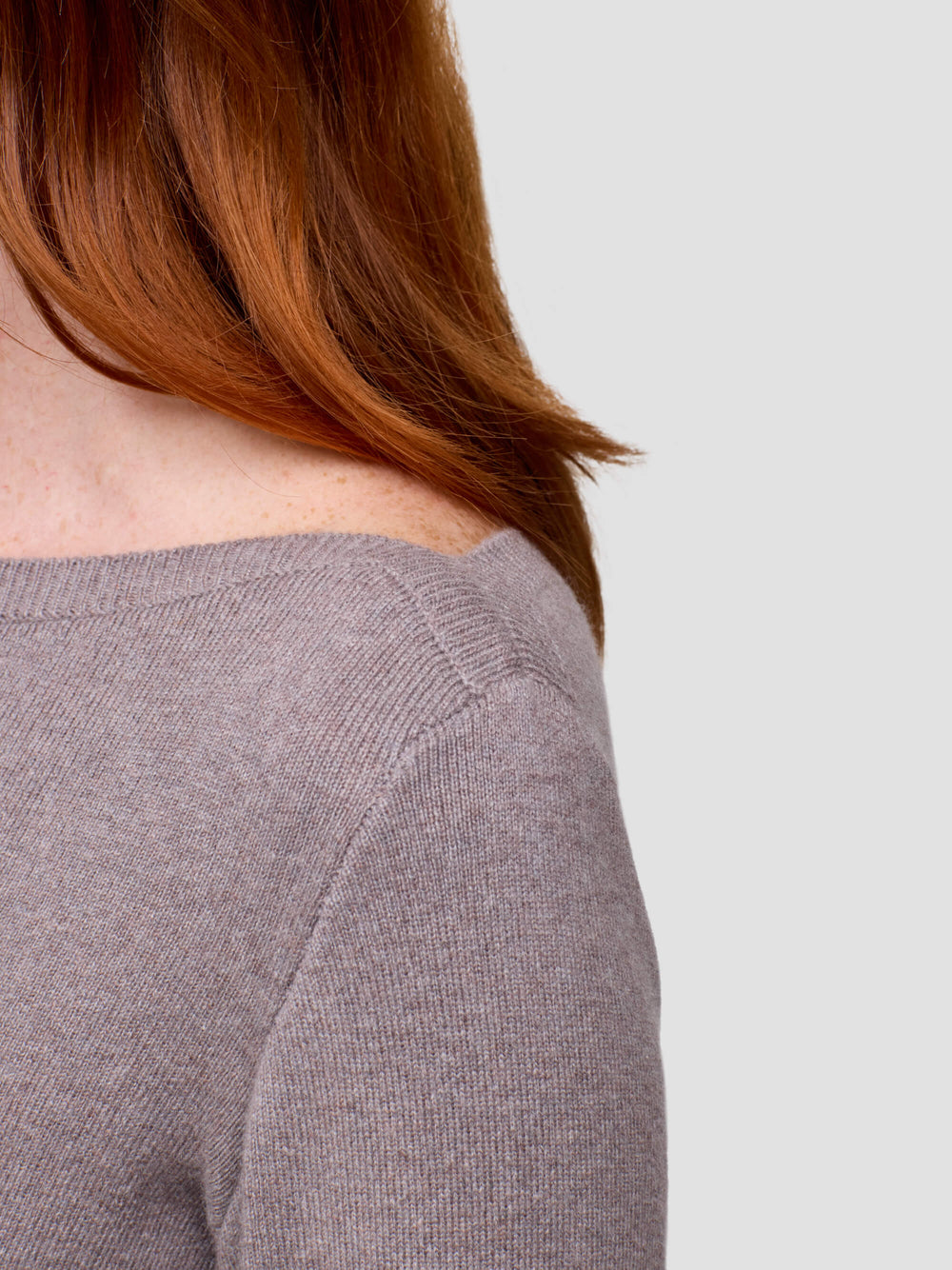 Woman wearing a grey long-sleeve cashmere dress against a plain background