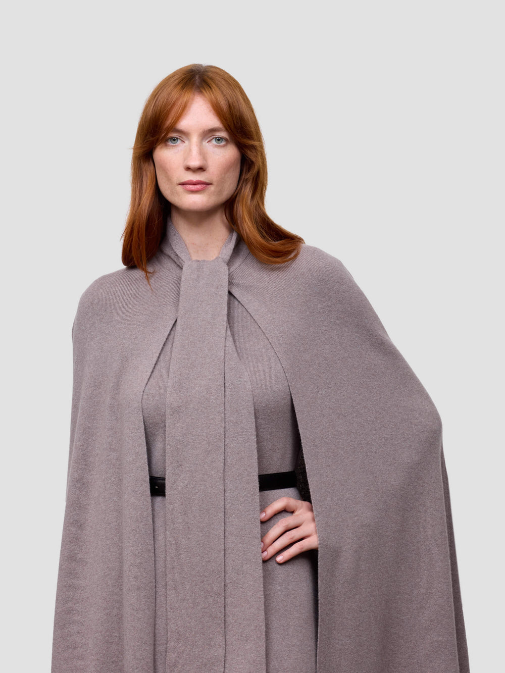 Woman wearing a long gray cashmere cape with a plain background
