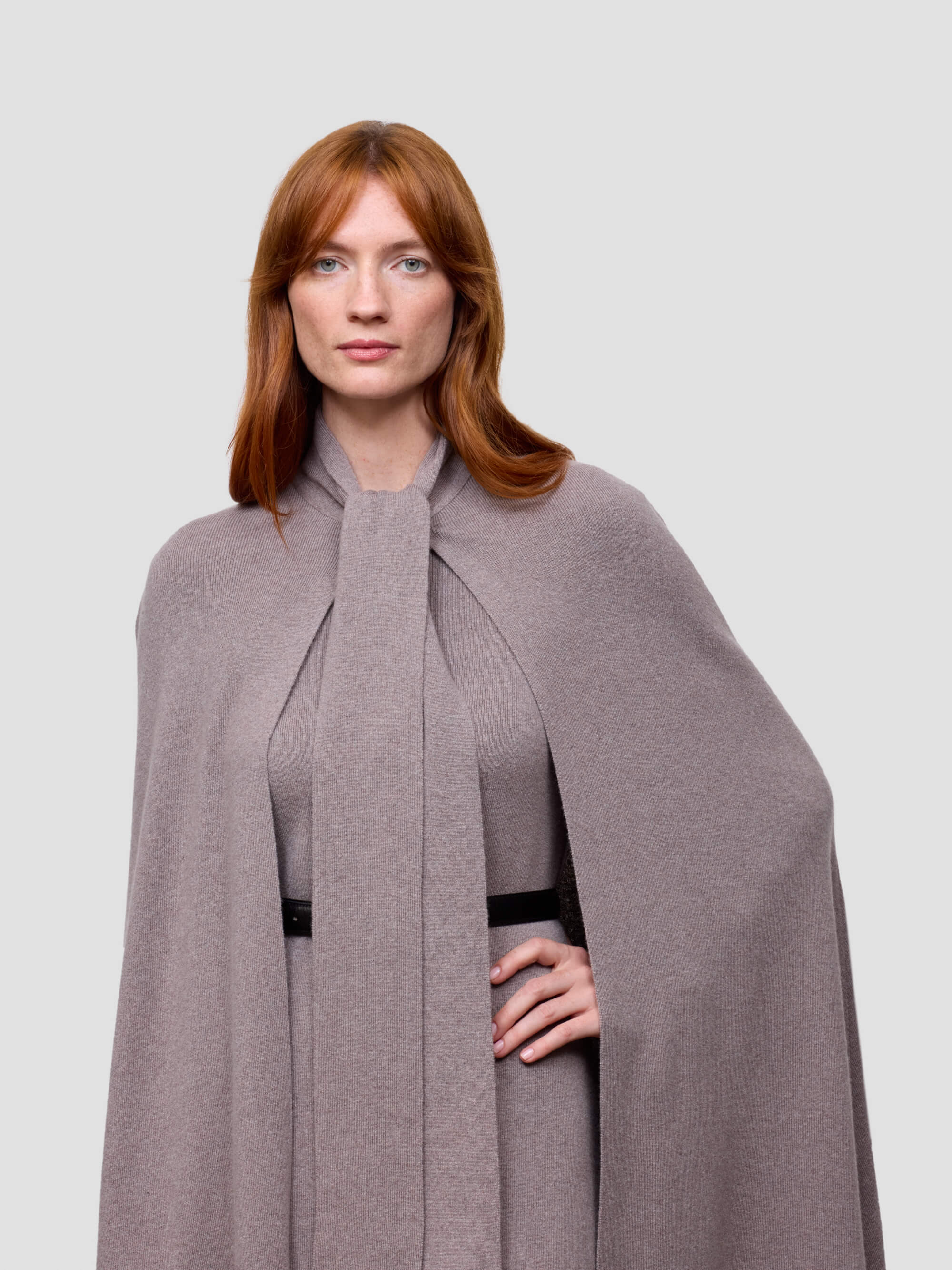 Woman wearing a long gray cashmere cape with a plain background