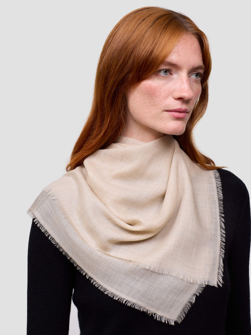 Woman wearing a beige cashmere scarf on a plain background