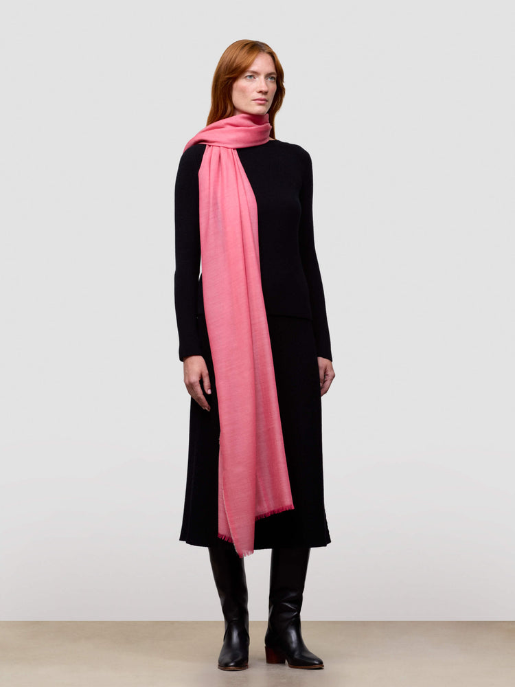 Woman wearing a black cashmere dress and pink cashmere scarf on a white background