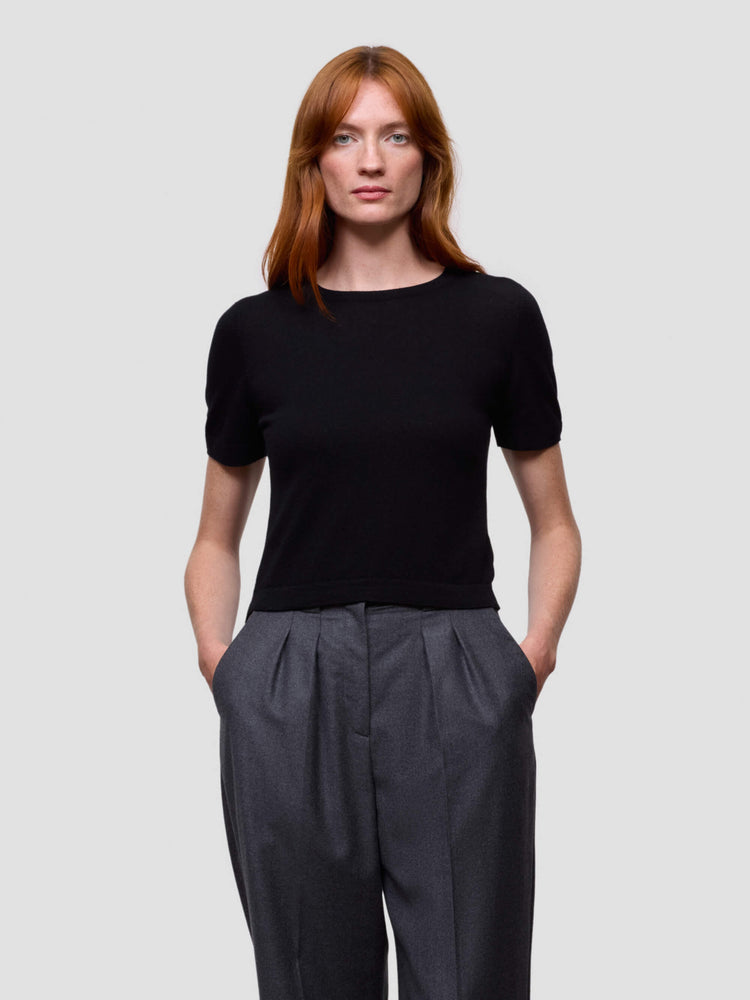 Woman wearing a black cashmere tshirt and dark gray pants against a light gray background