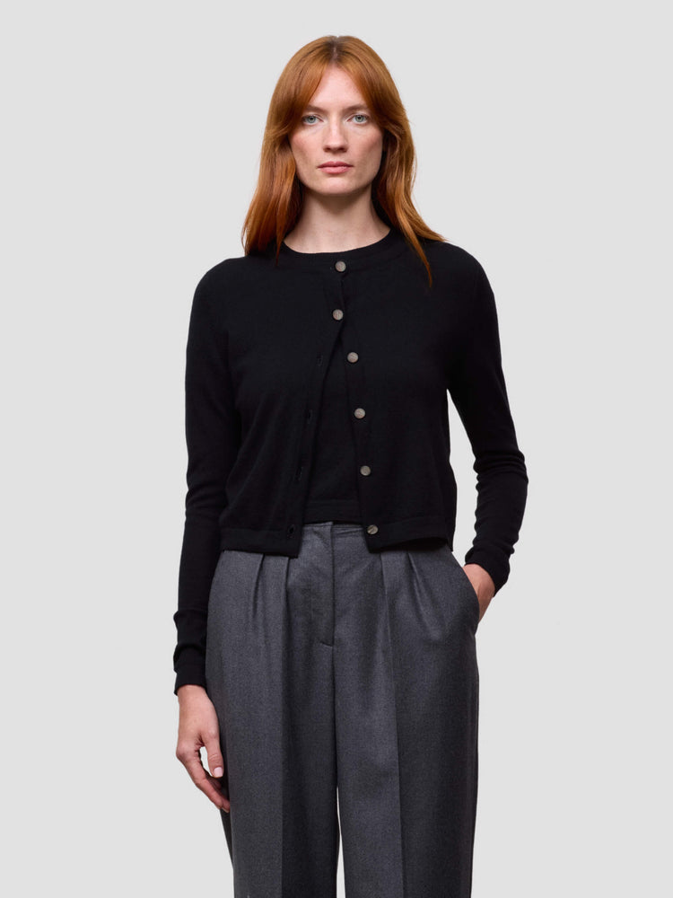 Woman wearing a black cardigan and gray pants on a light gray background