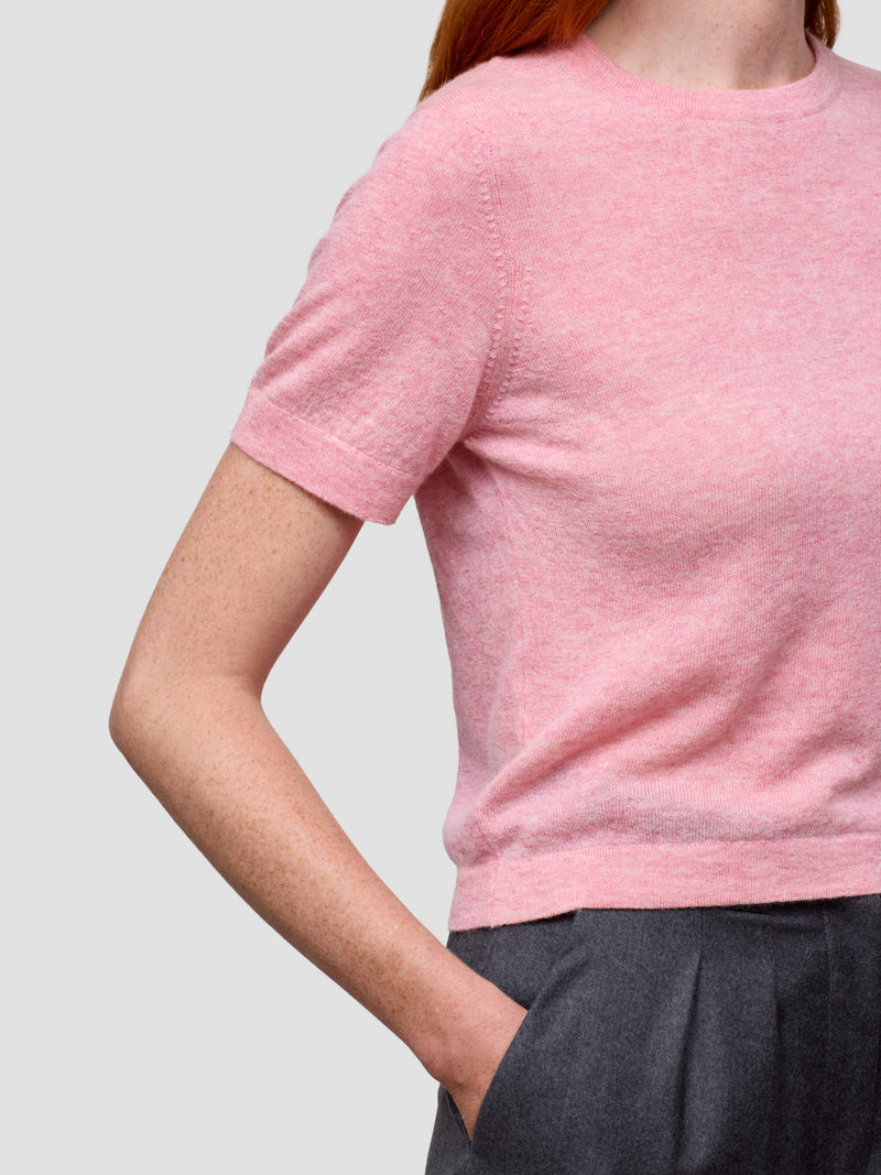 Person wearing a pink short-sleeve shirt against a plain background