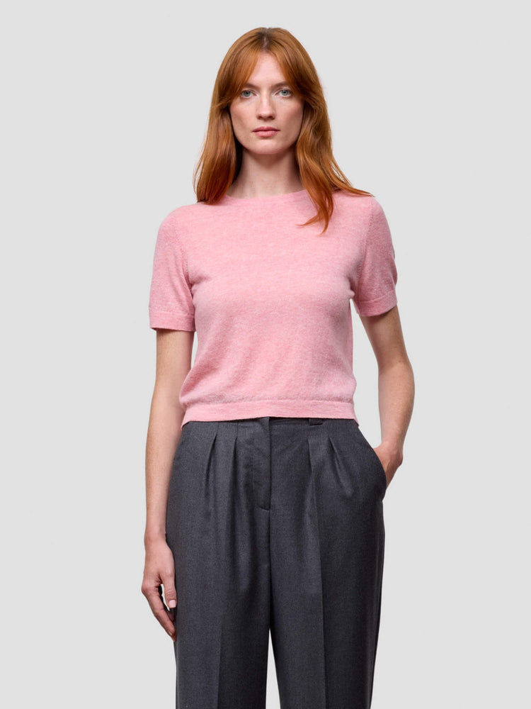 Woman wearing a pink cashmere tshirt and dark pants on a light gray background