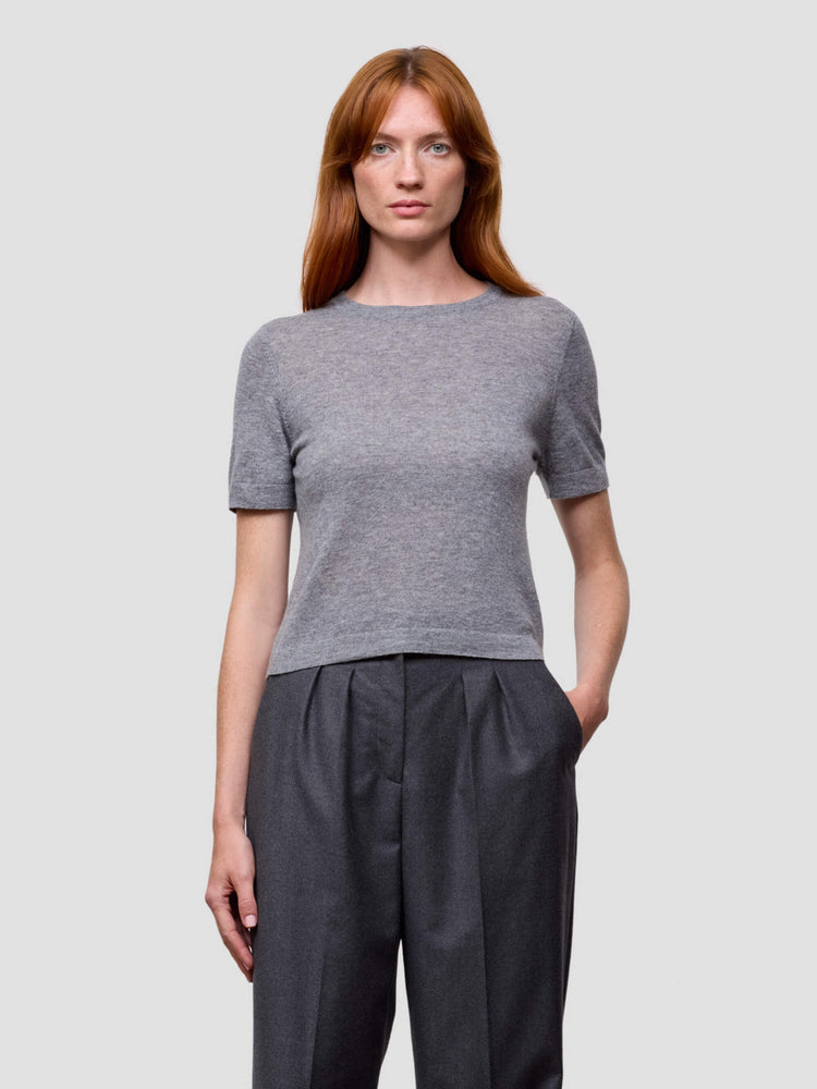 Woman wearing a gray cashmere short-sleeve top and dark pants on a light gray background