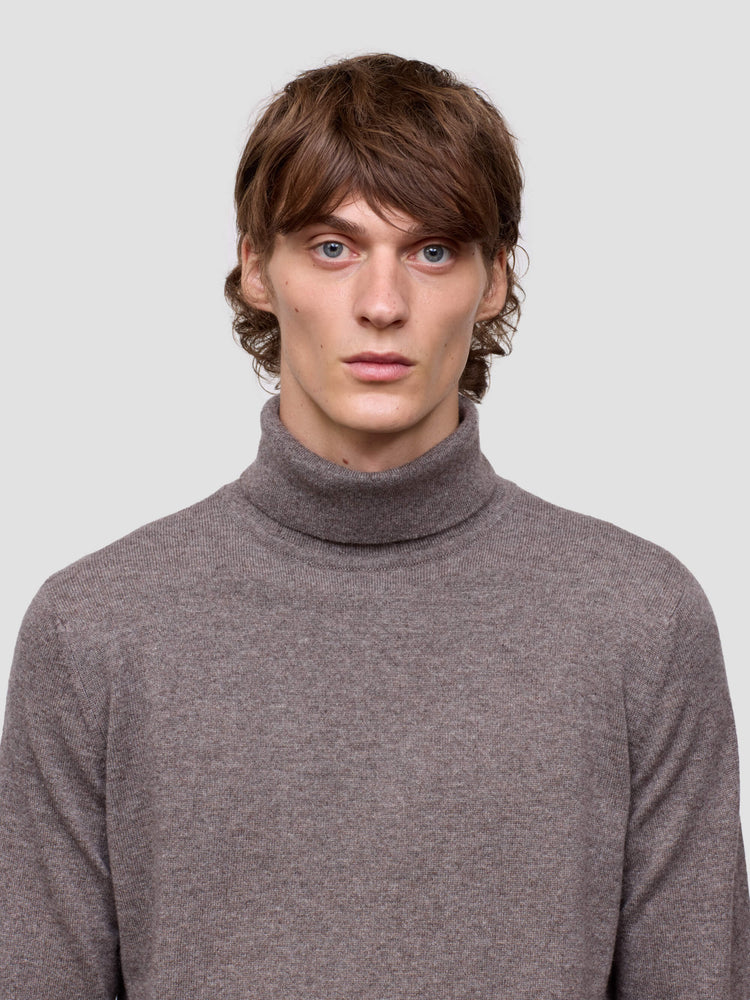 Man wearing a brown turtleneck sweater against a plain background