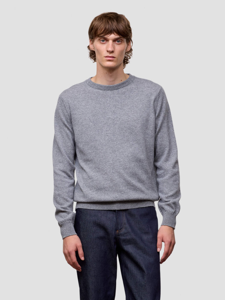 Man wearing a gray cashmere sweater and dark pants on a light gray background