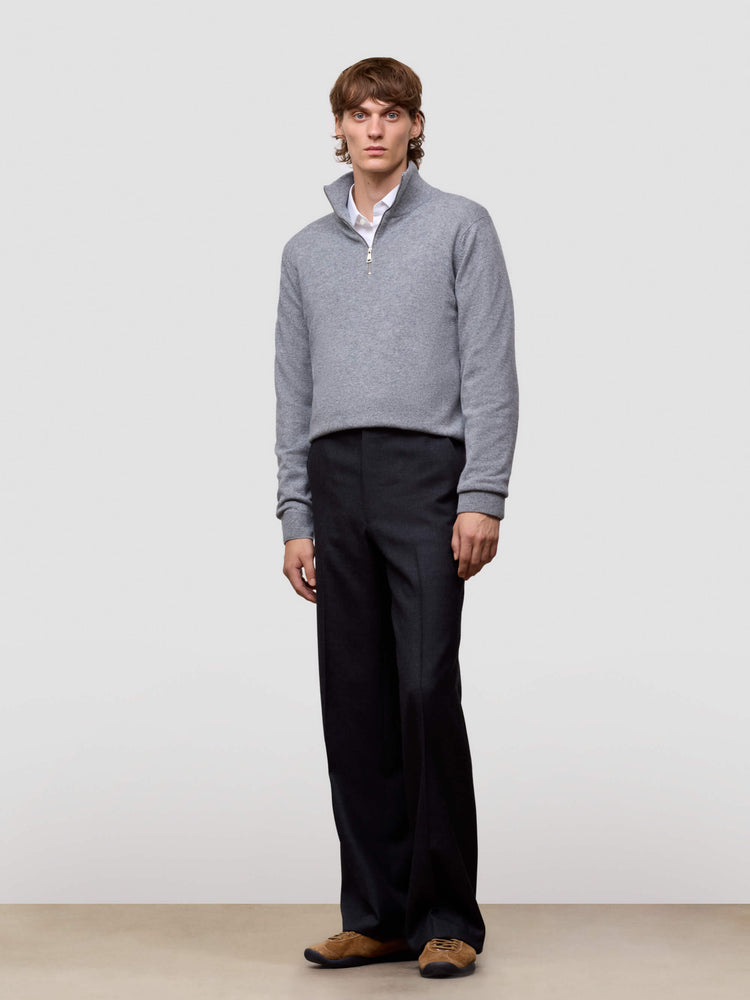 Man wearing a gray half zip sweater and black pants against a white background