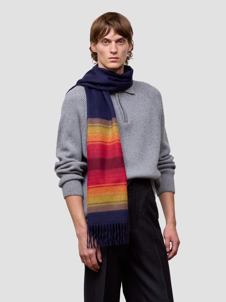man wearing a grey zip jumper and striped navy and red cashmere scarf on plain background