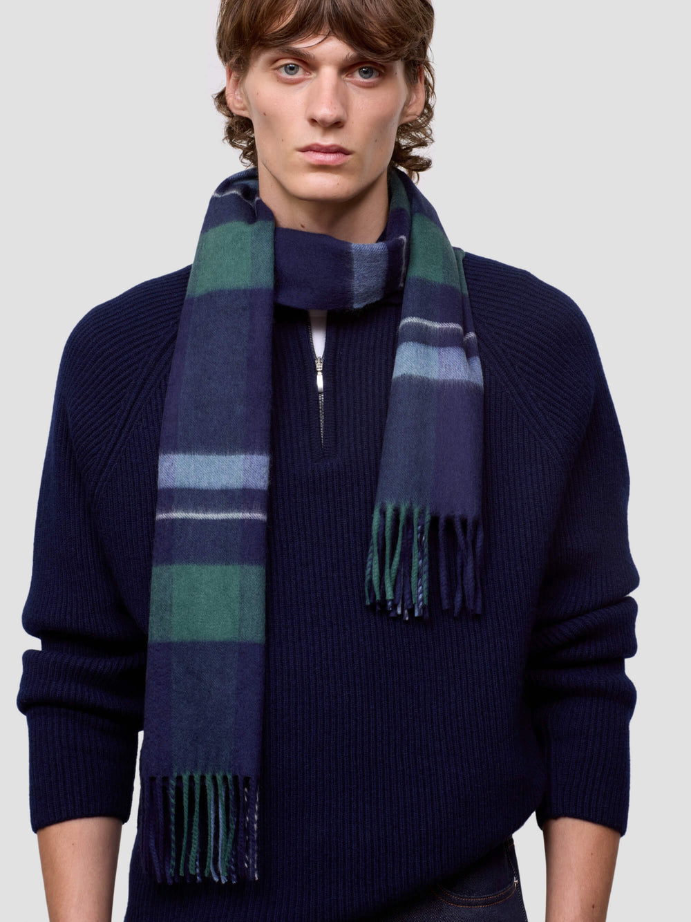 Man wearing a navy sweater and a striped scarf on a light gray background