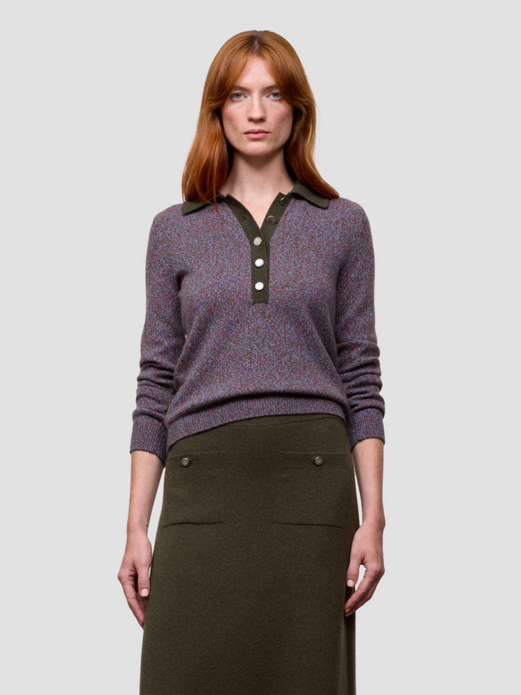 Woman wearing a purple sweater with black collar and buttons, standing against a plain background