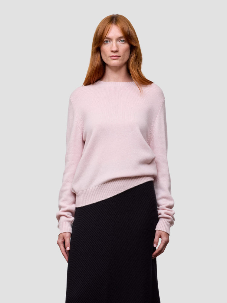 Woman wearing a light pink cashmere sweater and black skirt on a white background