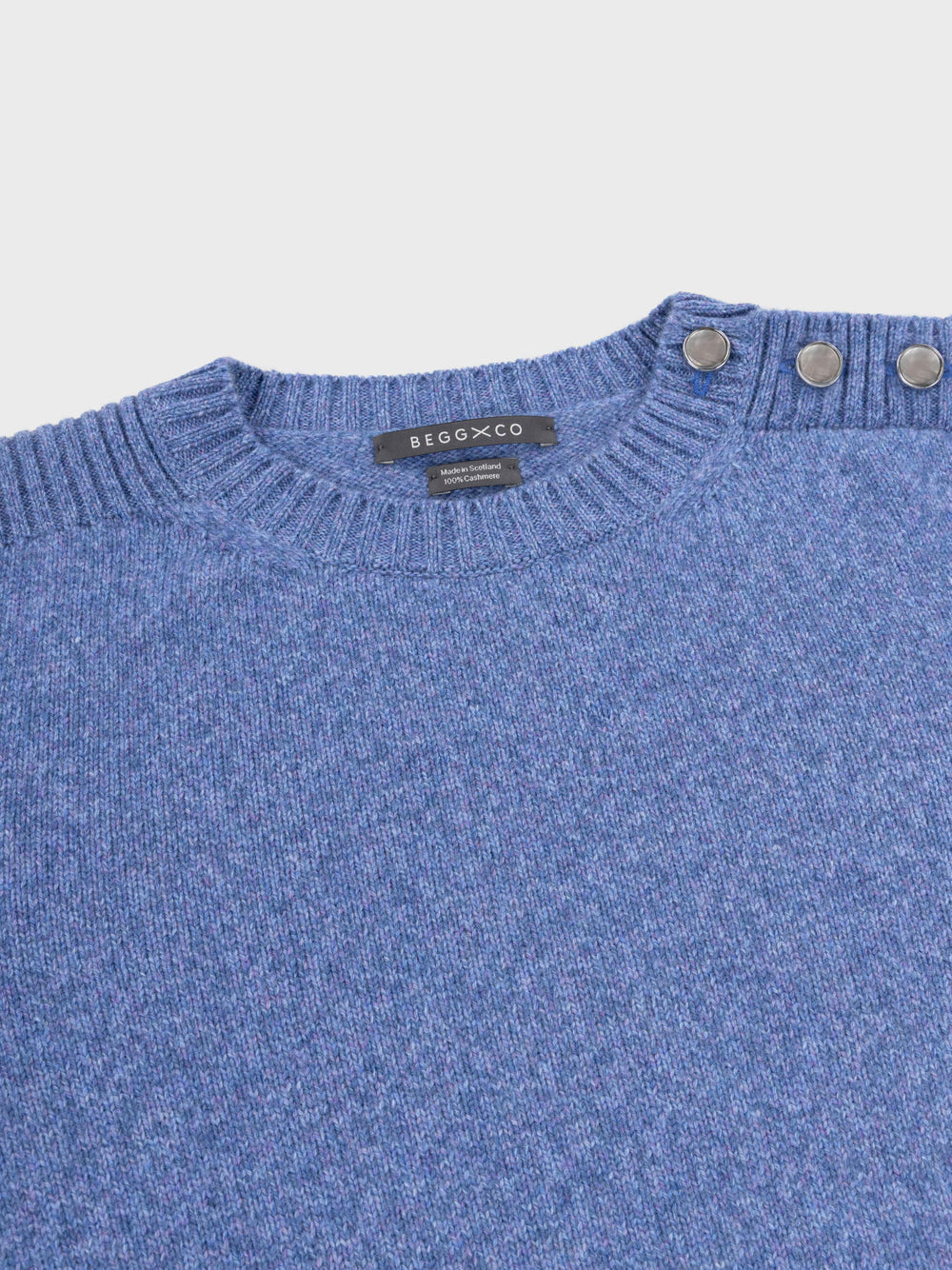 denim blue cashmere crew neck sweater with pearl button shoulder details on a grey background