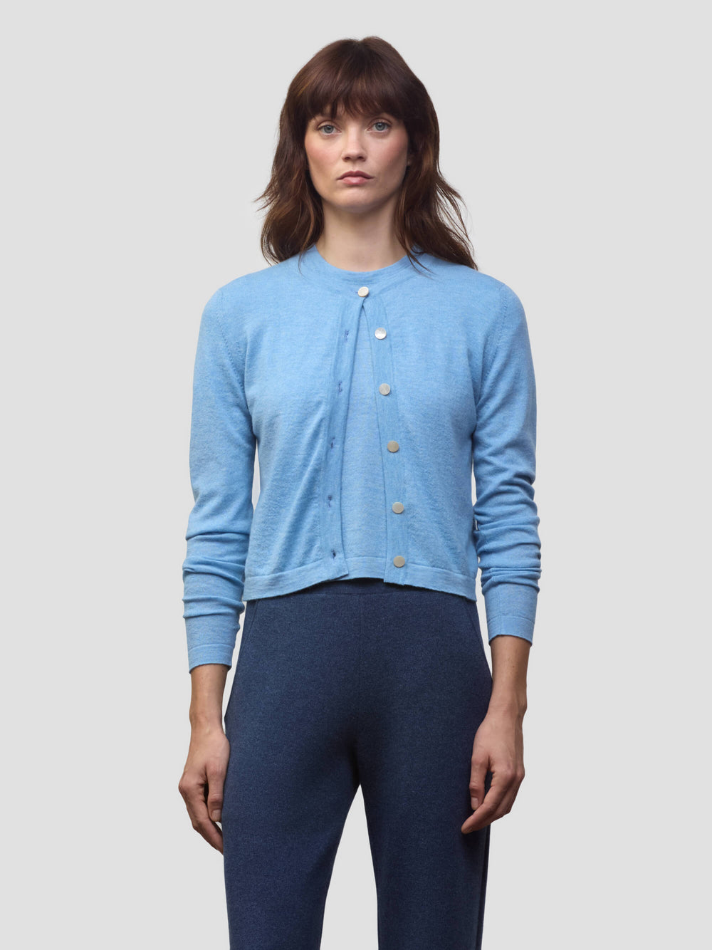 Woman wearing a blue cashmere cardigan over dark blue cashmere trousers on a light gray background