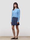 Woman wearing a blue cashmere cardigan over a dark blue cashmere skirt on a light gray background