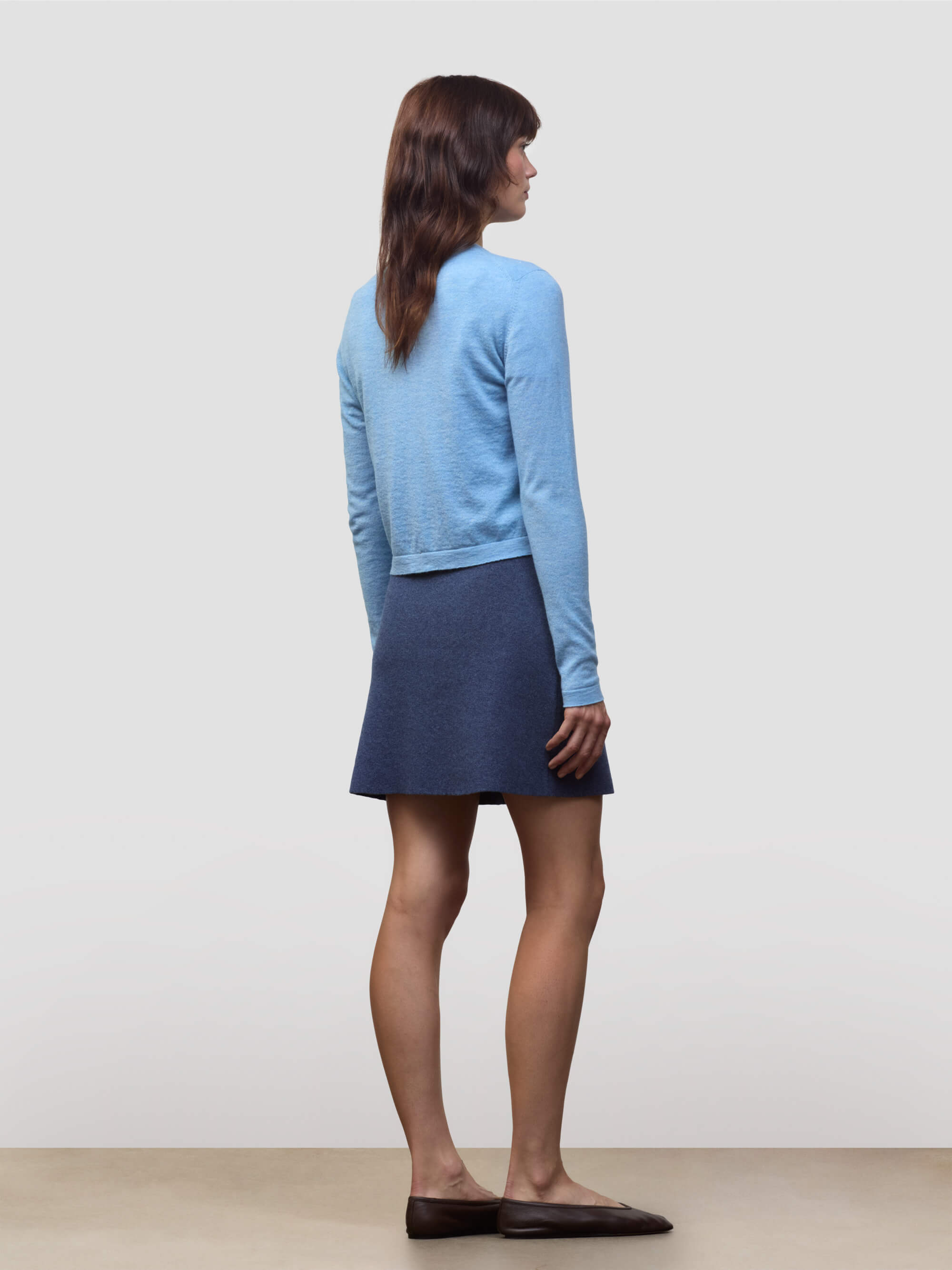 Woman wearing a blue cashmere cardigan over a dark blue cashmere skirt on a light gray background