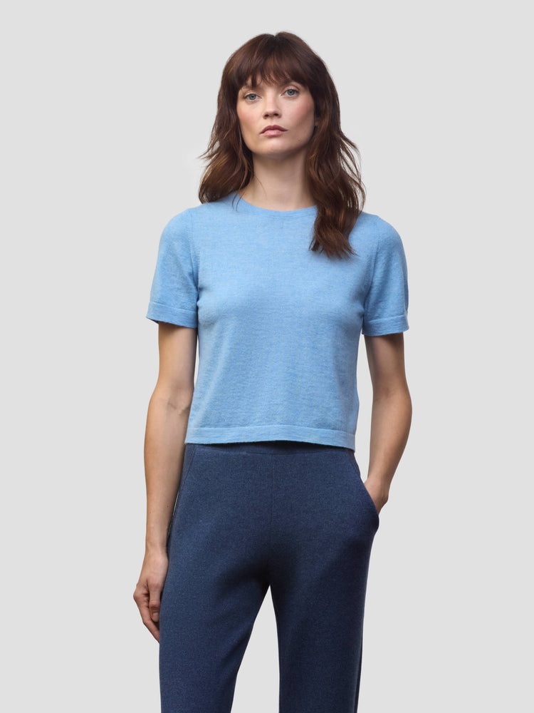 Woman wearing a light blue cashmere tshirt and dark blue cashmere pants on a plain background