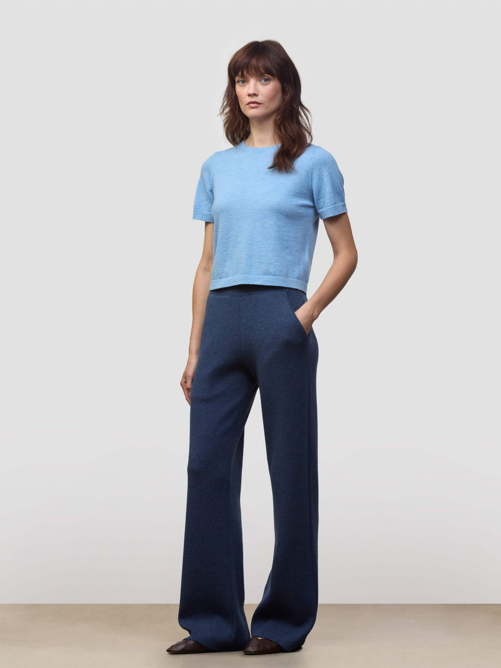 Woman wearing a light blue cashmere tshirt and dark blue cashmere pants on a plain background