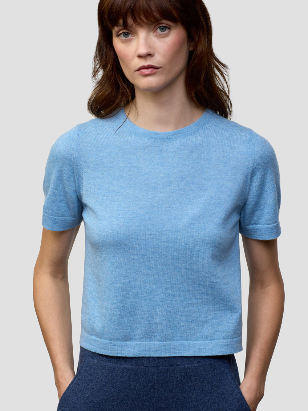 Woman wearing a light blue cashmere tshirt and dark blue cashmere pants on a plain background