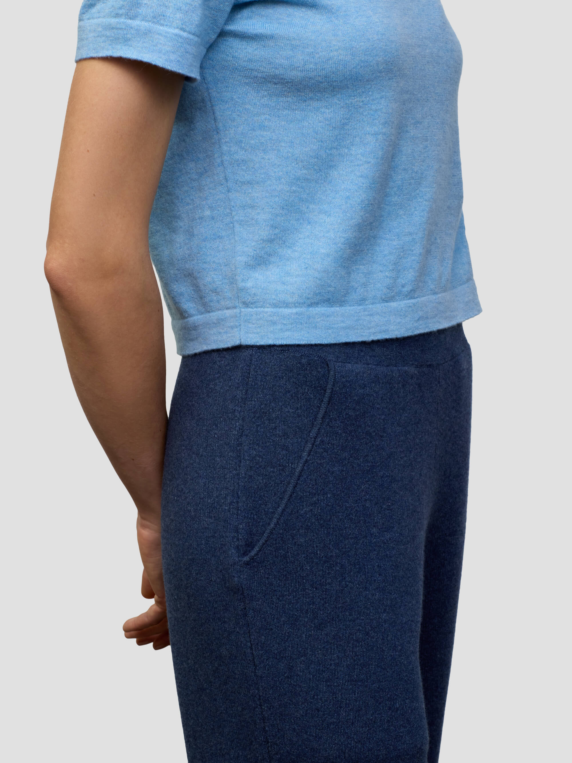 Woman wearing a light blue cashmere tshirt and dark blue cashmere pants on a plain background