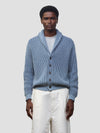 man wearing blue and navy ribbed cashmere cardigan with white shorts on a grey background