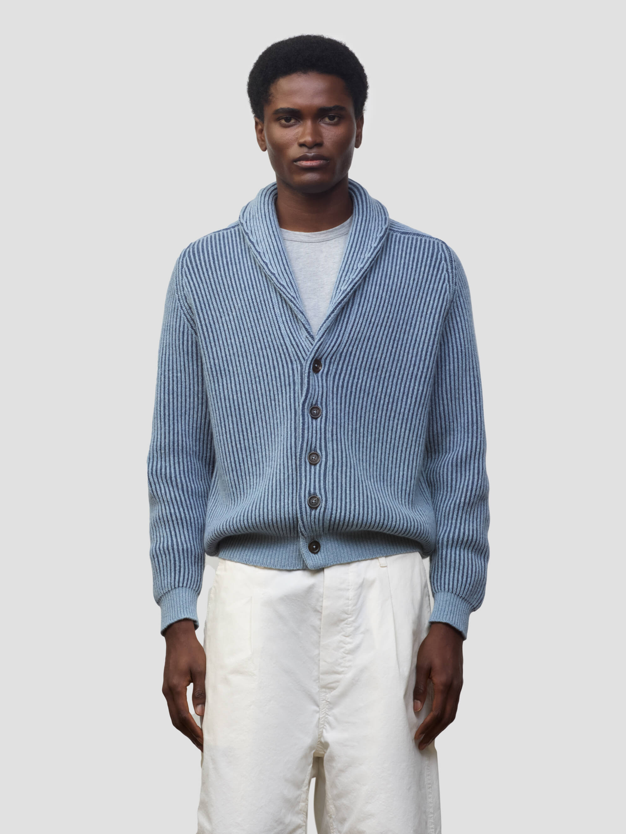 man wearing blue and navy ribbed cashmere cardigan with white shorts on a grey background
