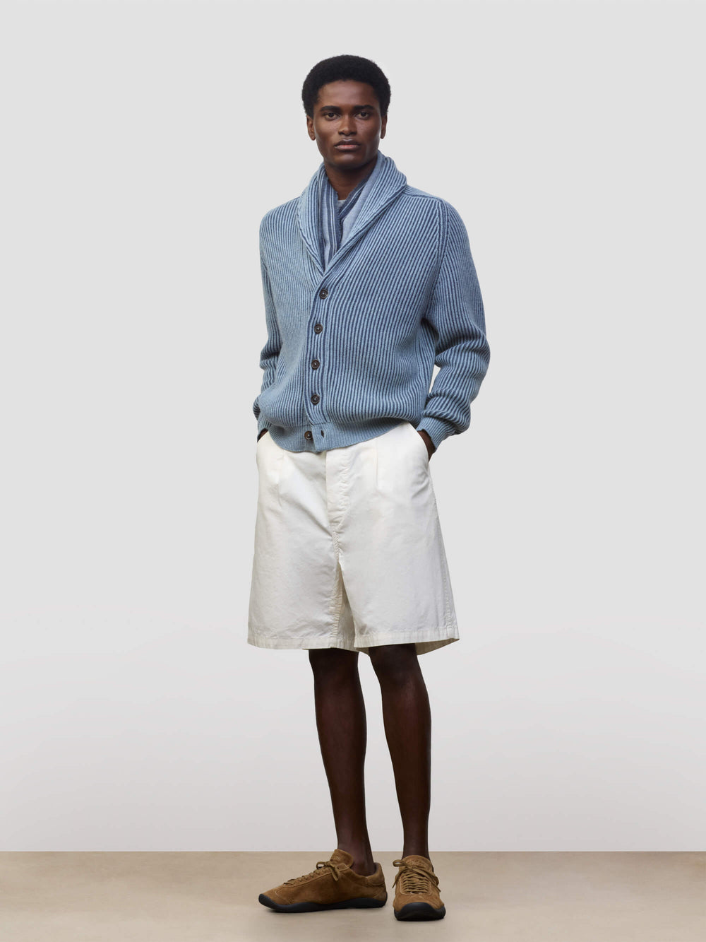 man wearing blue and navy ribbed cashmere cardigan with white shorts on a grey background
