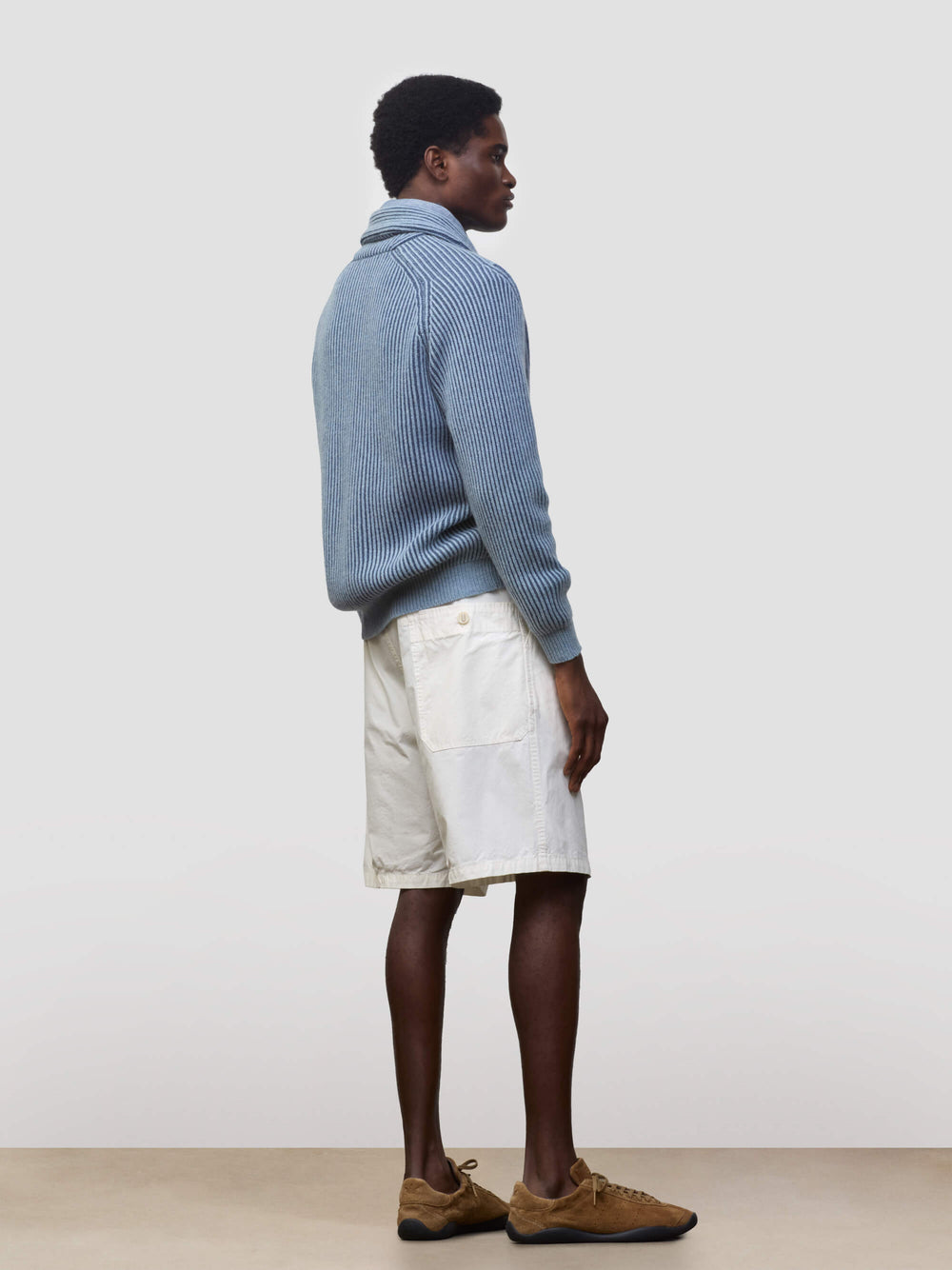 man wearing blue and navy ribbed cashmere cardigan with white shorts on a grey background
