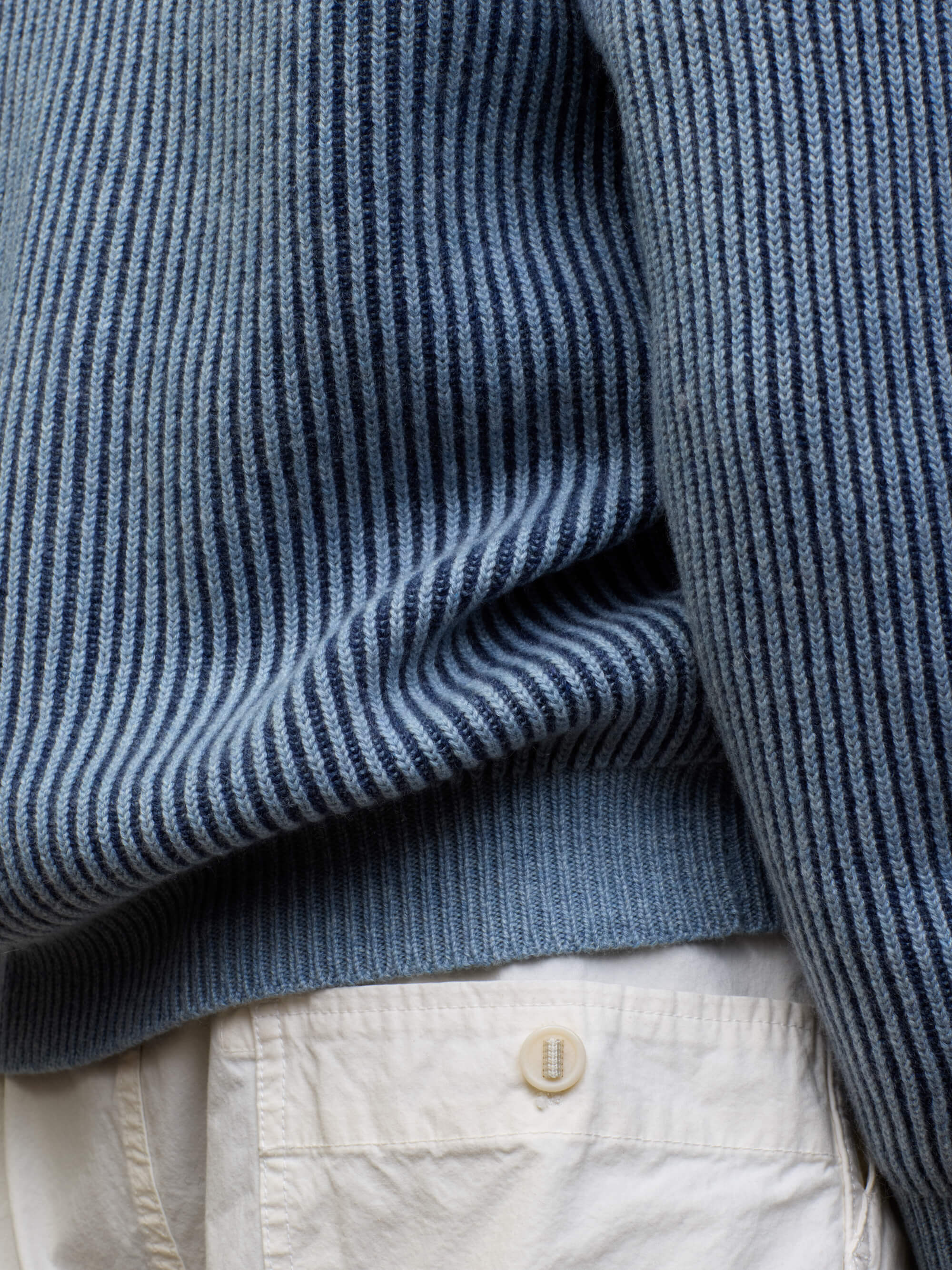 detail of a blue and navy ribbed cashmere cardigan with white shorts
