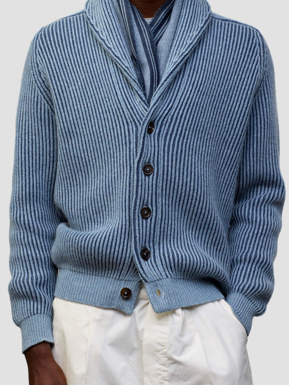 detail of a man wearing blue and navy ribbed cashmere cardigan with white shorts on a grey background