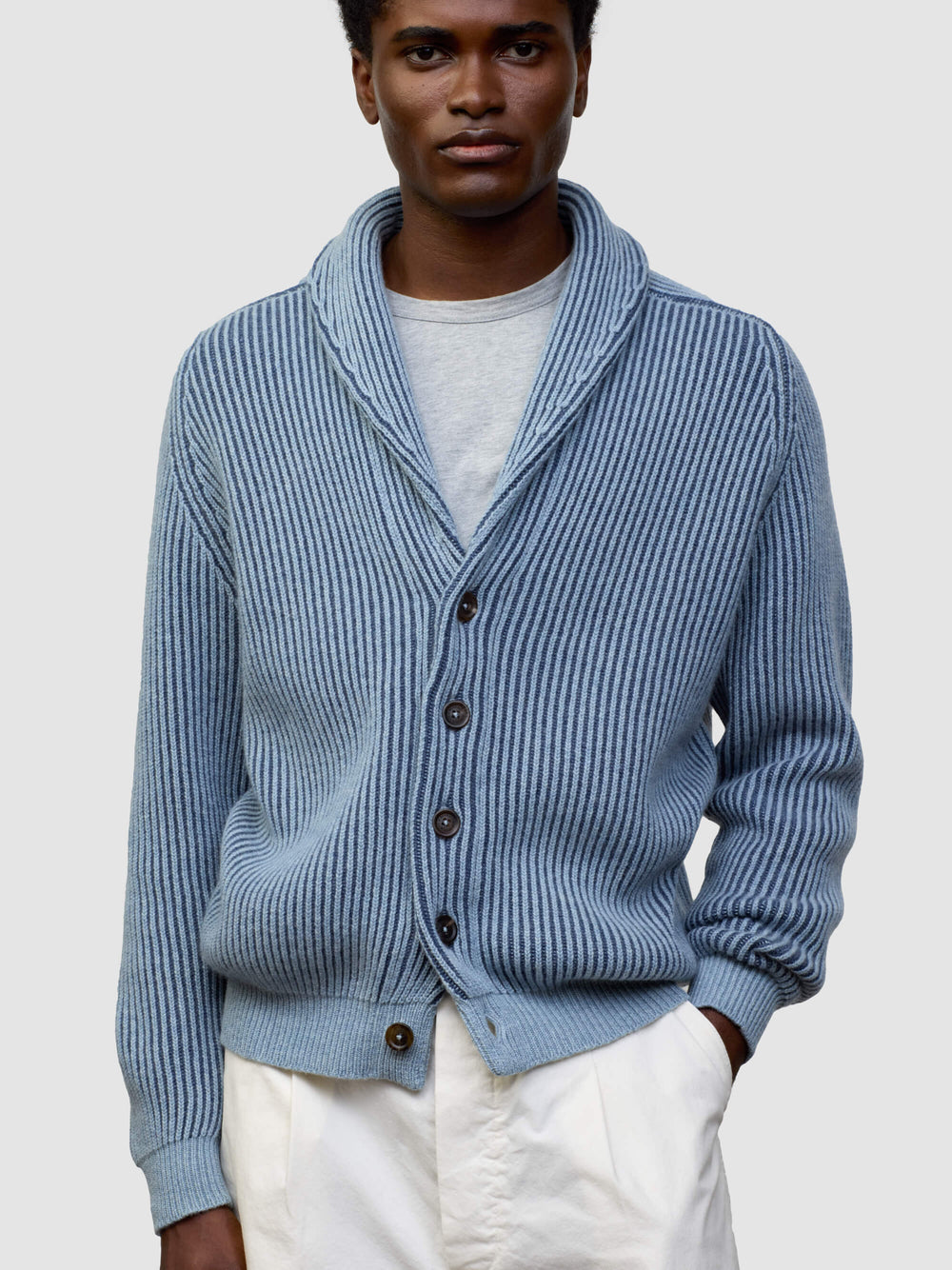 man wearing blue and navy ribbed cashmere cardigan with white shorts on a grey background