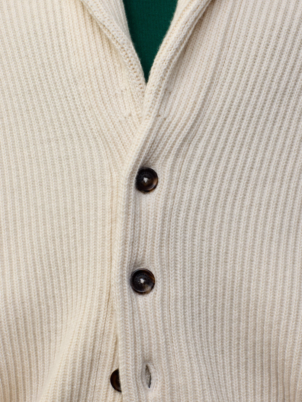 button detail of a man wearing a natural colour ribbed cashmere cardigan over a green tshirt 