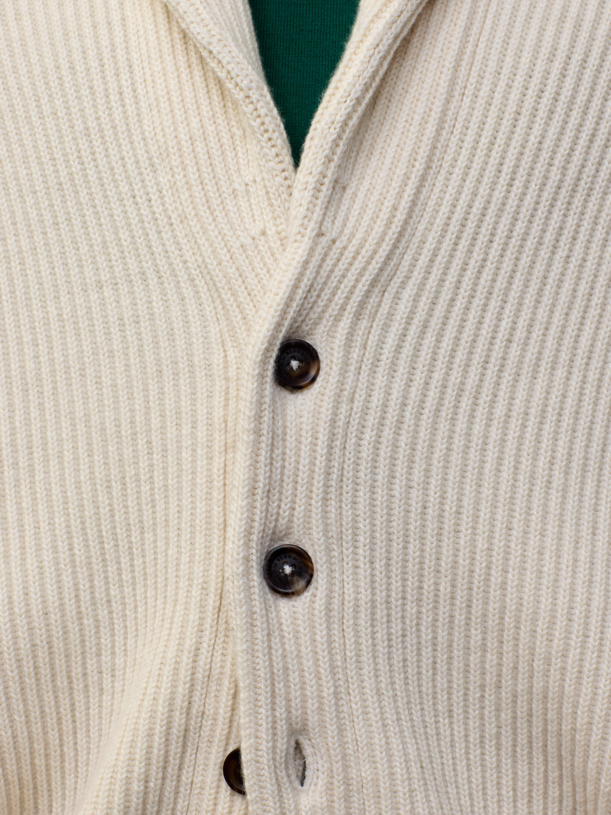 button detail of a man wearing a natural colour ribbed cashmere cardigan over a green tshirt 