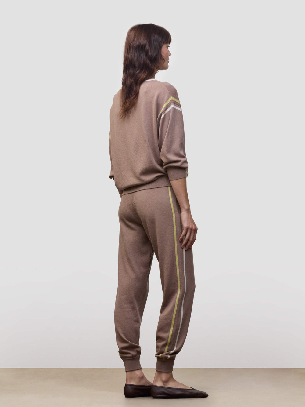 Woman wearing a brown cashmere loungeset with white and yellow stripes on a plain background