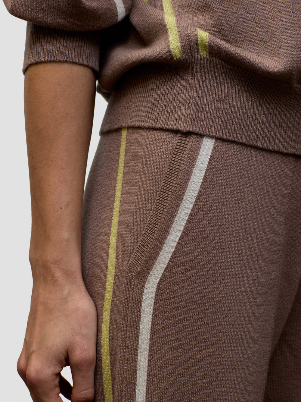 Woman wearing a brown cashmere loungeset with white and yellow stripes on a plain background